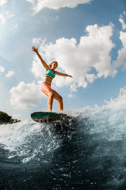年轻女子在冲浪板上玩水上冲浪，在蔚蓝的天空中荡漾着波浪图片下载