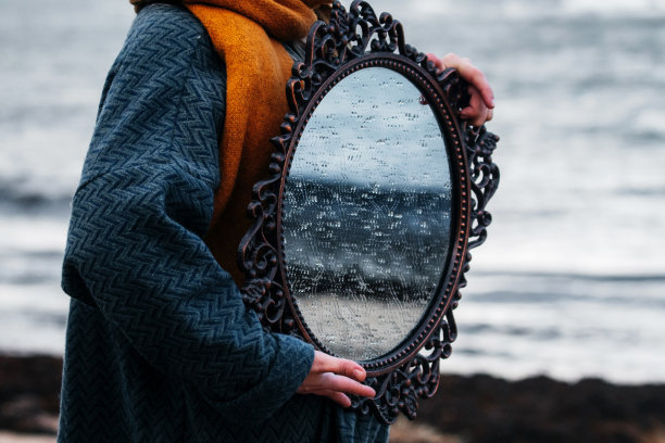 一个女人在海边拿着一面古董镜子。图片下载