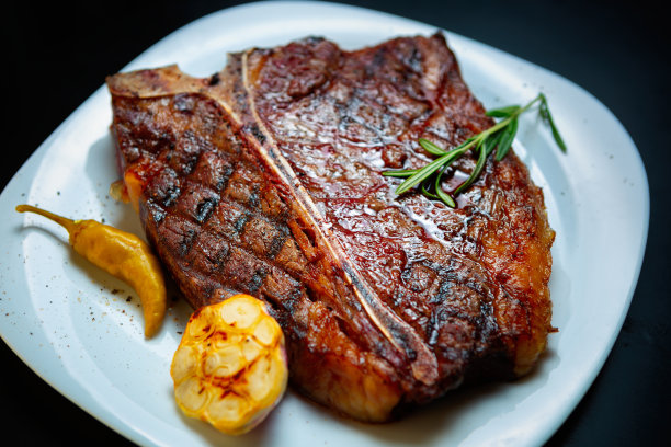 美国美食餐厅的t骨牛排。美味的牛排与蔬菜烤，并与迷迭香香草在白色盘子。为晚餐准备的红牛柳图片下载