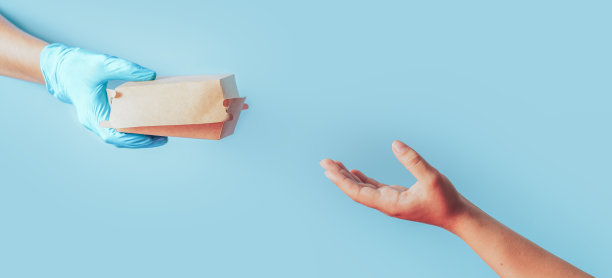 在蓝色的背景下，一只手戴着蓝色的手套将纸制的食物容器传递给另一只手图片下载