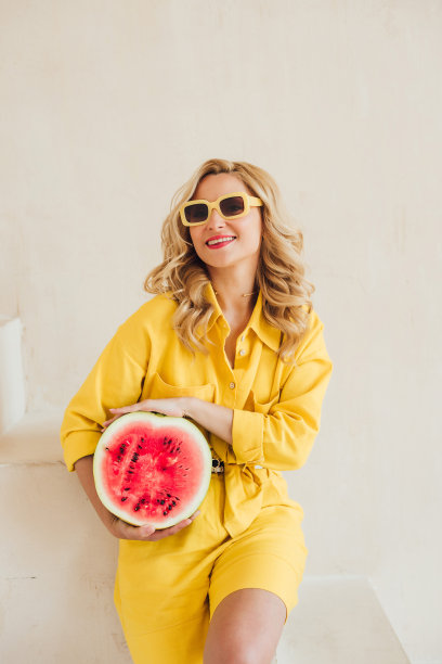 一个迷人的微笑女人的肖像，穿着黄色的夏装，戴着夏天的太阳镜，手里拿着一个多汁的西瓜。快乐的夏天，假期，灵感。软选择聚焦。图片下载