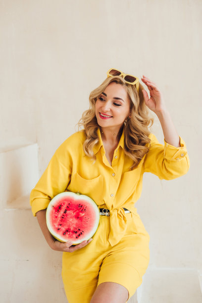 一个迷人的微笑女人的肖像，穿着黄色的夏装，戴着夏天的太阳镜，手里拿着一个多汁的西瓜。快乐的夏天，假期，灵感。软选择聚焦。图片下载