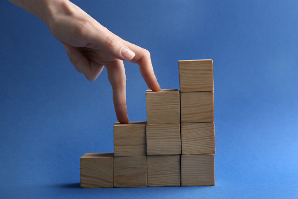 蓝色背景上木制立方体搭建的女人和楼梯，特写。职业晋升的概念图片下载