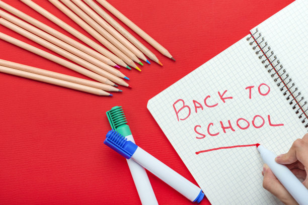 回到学校。孩子用红色记号笔在笔记本上写“回到学校”。学年开始的概念。红色背景上的网站横幅图片下载
