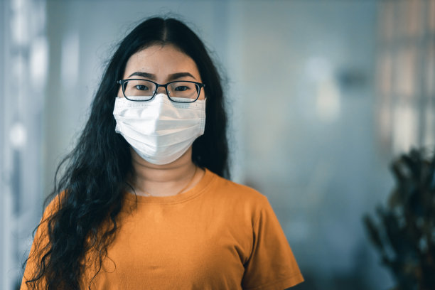 亚洲女性戴着卫生防护口罩，穿着橙色衣服，在咨询中看着摄像机的肖像，新冠病毒的概念图片下载
