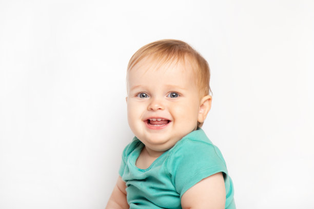 穿着绿色t恤的小男孩开心地笑着，看着被隔离在白色背景下的相机。儿童保育和养育的概念。图片下载