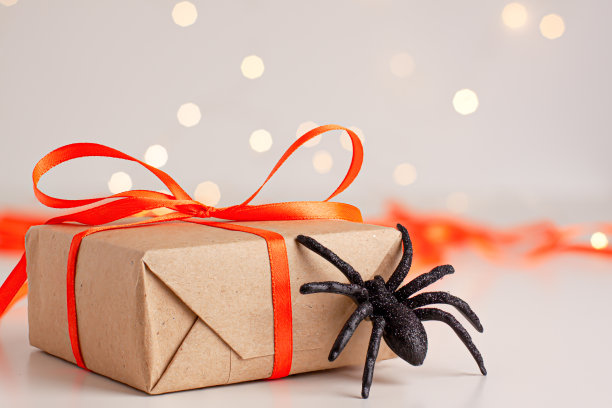 特写的棕色礼盒与橙色缎带蝴蝶结和黑色恐怖蜘蛛明亮模糊的背景与bokeh复制空间。秋天节日的概念图片下载