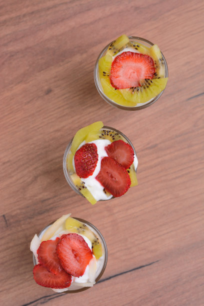 水果甜点与酸奶和水果在玻璃杯。在木头表面，俯视图。图片下载