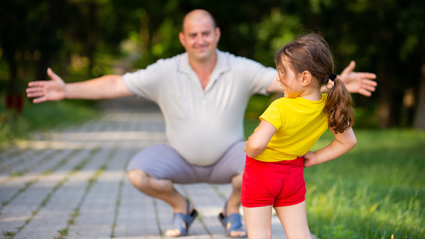 快乐的爸爸蹲在他的膝盖上微笑着，他想用爱拥抱他的女儿，一起在公园度过美好的时光。图片下载