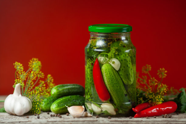 玻璃罐里的腌黄瓜和红色背景下准备腌黄瓜的香料和蔬菜图片下载