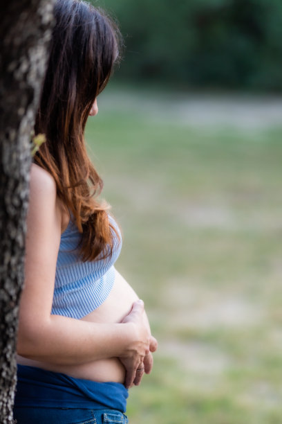 一名孕妇倚在公园的一棵树上的侧面垂直照片图片下载
