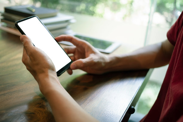 咖啡店里，一名男子手拿着一部带有Mockup的智能手机，屏幕黑黑的。近距离图片下载