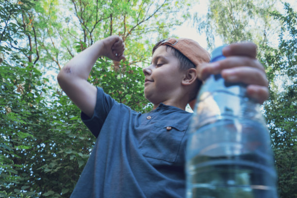 一个可爱的男孩拿着一瓶干净的水，展示他的二头肌图片下载