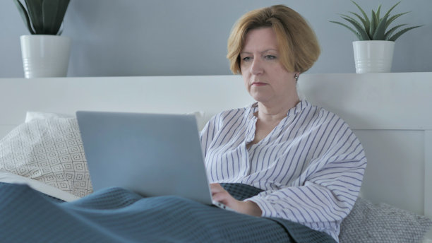 躺在床上休息的老妇人在笔记本电脑上工作图片下载