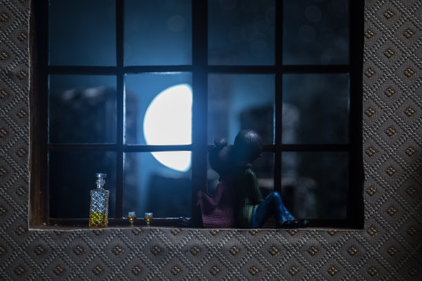 一个逼真的玩具屋客厅，在晚上有家具和窗户。一对浪漫的情侣坐在窗户上。艺术品桌子装饰与手工制作的现实的娃娃屋。有选择性的重点。图片下载