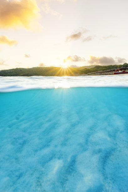 (选择性对焦)分割拍摄，在图片下面。清澈碧绿的海水和一些沙滩伞在令人惊叹的日出中被照亮。意大利撒丁岛的大佩维罗海滩。图片下载