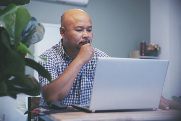 亚洲高级男子在家庭办公室的笔记本电脑上打字。严肃的金融男性使用电脑在线工作，穿着休闲。技术的概念。图片下载