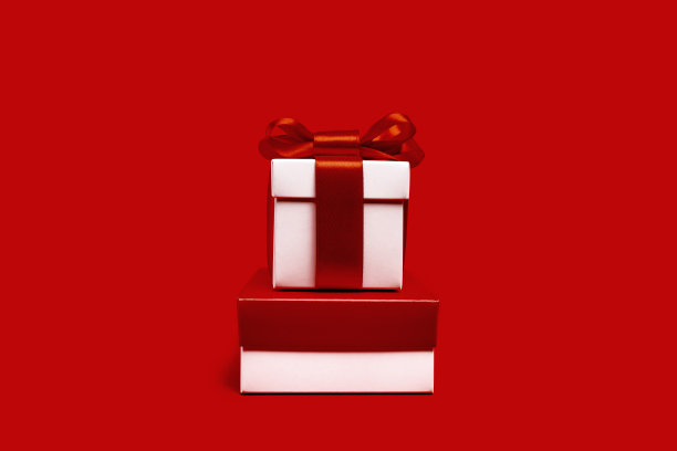 一个白色礼品盒，红色背景上有蝴蝶结图片下载