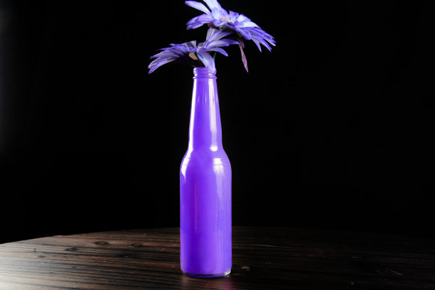紫色瓶子与蓝色的花朵孤立在黑色的背景。图片下载