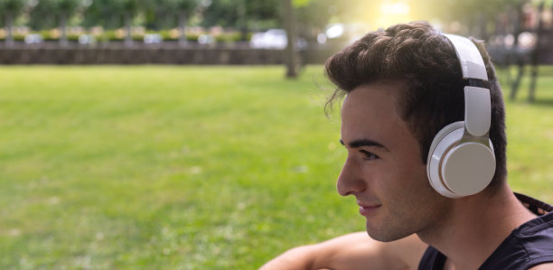 一个运动男孩通过白色头盔在公园花园中间放松地听音乐的细节图片下载