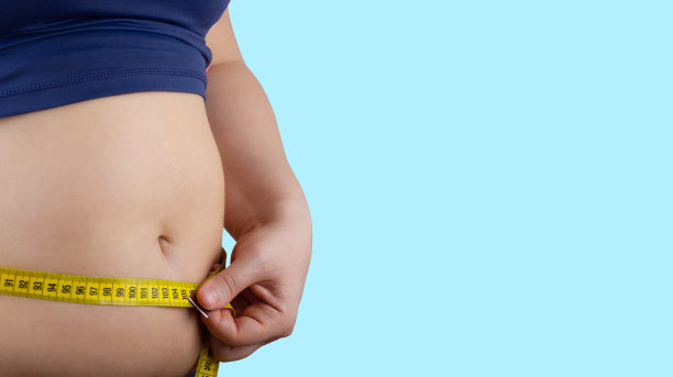 超重女子用卷尺量腰，横着，复制空间，孤立在蓝色上图片下载