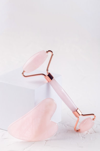 粉彩石英水晶面部滚轮和按摩工具刮沙上白色背景，垂直，复制空间图片下载