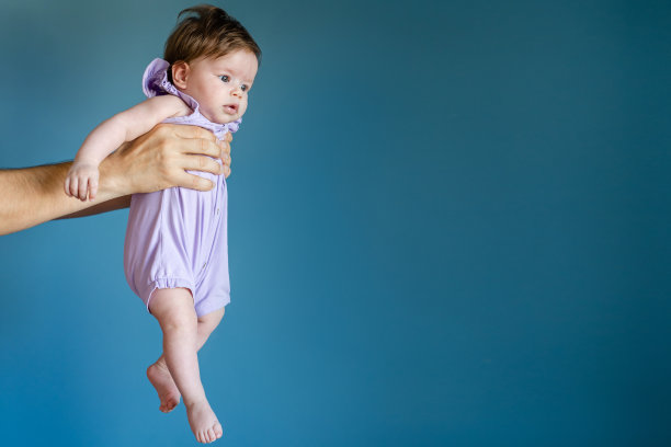 陌生男人的双手，父亲抱着他的宝贝女儿，女孩在蓝色的墙上，在空中，孩子穿着紫色的衣服，在夏天的日子，养育和父亲的概念，成长复制空间图片下载