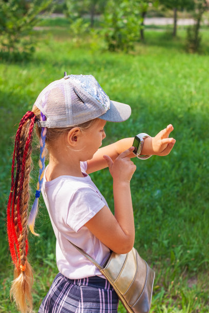 小孩在户外使用智能手表。孩子在用智能手机说话。一名女学生在手表上使用触摸屏浏览互联网图片下载