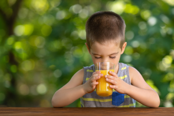 小男孩喝着玻璃杯里的橙汁图片下载
