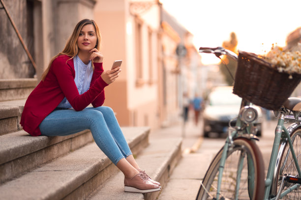 时髦的女人骑着自行车坐在楼梯上用手机图片下载