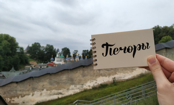 View to Pskov-Pechory Orthodox male Monastery with calligraphy题字“Pechory”in russian on notebook。俄罗斯普斯科夫州佩霍里，2021年7月30日。——在笔记本上。移动摄影。图片下载