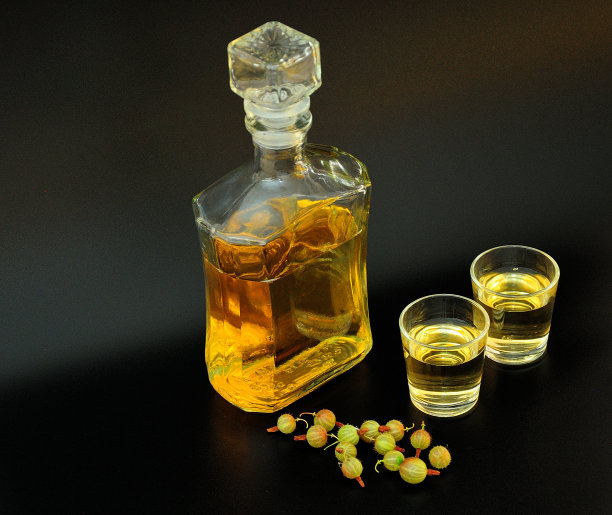 自制的绿色醋栗利口酒，一个瓶子和两个杯子，黑色背景，旁边是一把成熟的浆果。图片下载