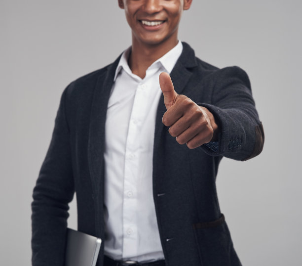 摄影棚里，一个年轻的商人在灰色的背景下竖起大拇指图片下载