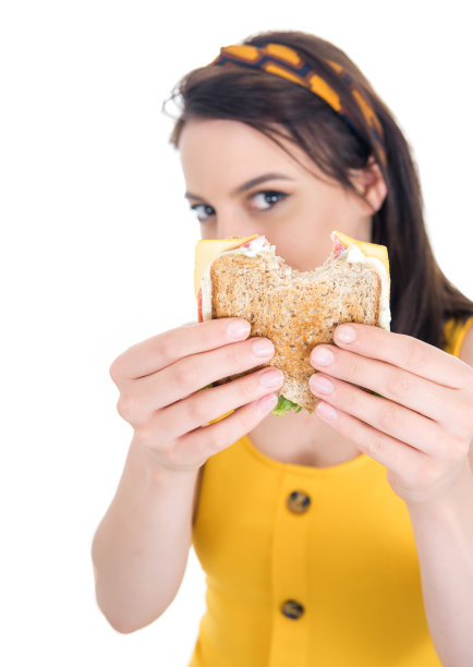 特写一位正在吃三明治的年轻女子。美丽的女孩享受在快餐，美味的小吃，孤立在白色的背景图片下载