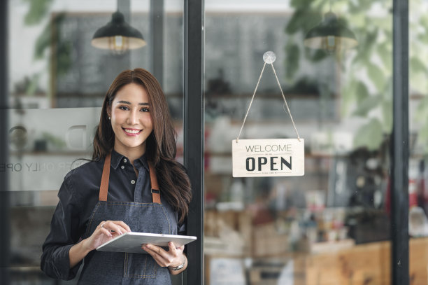 年轻美丽的女咖啡师站在咖啡馆前面的开放的牌子。图片下载