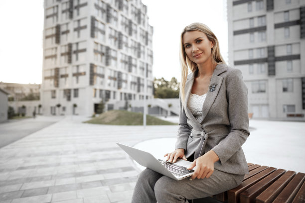 年轻漂亮的女商人坐在街上的长椅上用笔记本电脑工作图片下载