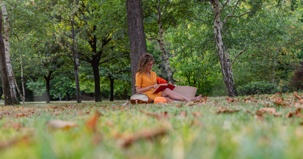一个年轻的卷发女人的库存摄影，享受她的自由时间和阳光灿烂的一天，在外面野餐，看书。图片下载