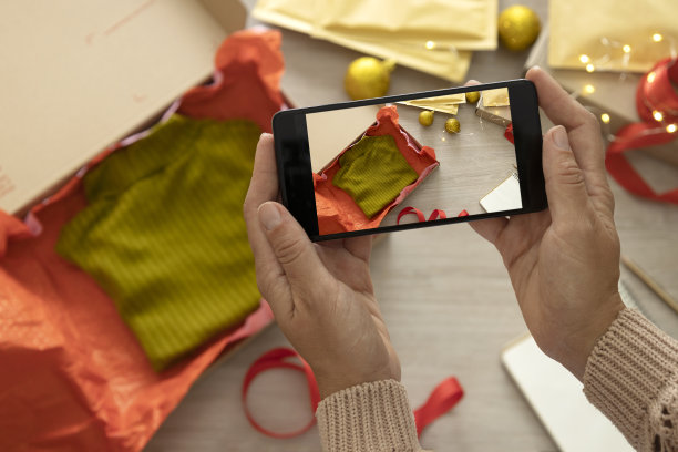 女人手拿智能手机，为节日餐桌拍照，包装礼物，在博客上分享照片。网上时尚圣诞销售，网上商务图片下载