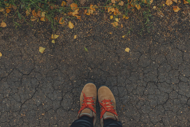 脚穿着棕色的靴子，踩在枯黄的落叶碎裂的地上。秋天的背景。生活方式的概念图片下载