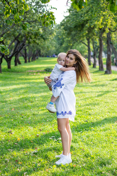 阳光明媚的日子里，母亲和她的儿子在公园里穿着白色的衣服，手牵着手，玩耍和拥抱图片下载