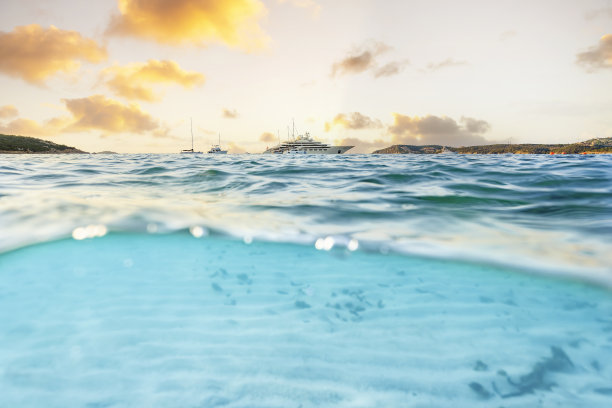 (选择性对焦)分割拍摄，在图片下面。在美丽的日出中，一艘豪华游艇在蓝绿色的海面上航行，半在水下半在天空。意大利撒丁岛的大佩维罗海滩。图片下载