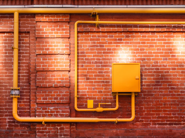 红色的砖墙，黄色的煤气管和阳光。有阳光反射的旧墙。表面破旧的旧建筑。图片下载