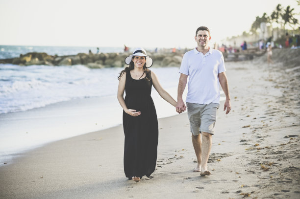 怀孕的妻子、妻子和丈夫沿着田园诗般的海滩散步图片下载