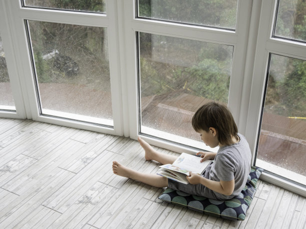 孩子坐在地板上看书。外面下雨的时候，孩子们的智力休闲。图片下载