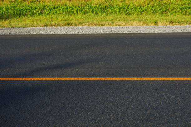 一条崭新的柏油路和一条黄色的分隔带。绿草长在路边。温暖阳光下的夏日风景图片下载