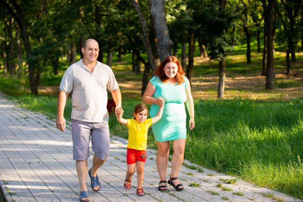 幸福的三口之家牵着女儿的手走在森林里，孕妇小心翼翼，男人轻手轻脚。图片下载