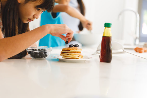 亚洲女儿在厨房准备早餐煎饼，哥哥在后面图片下载