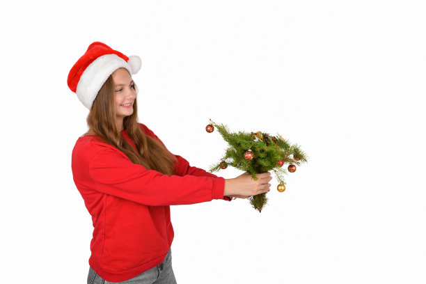 快乐的女孩戴着圣诞老人的帽子，穿着红色的有圣诞树树枝的套头衫图片下载