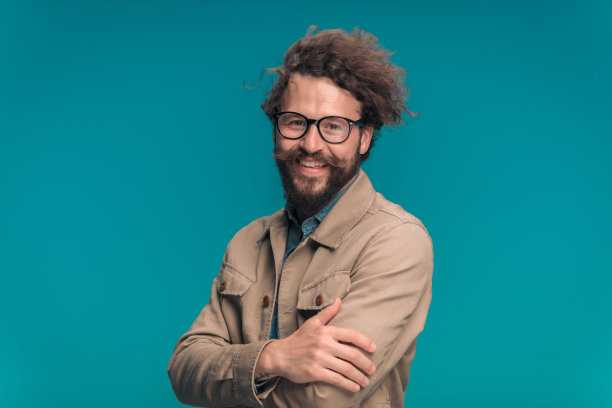 留着胡子的休闲模特穿着米色夹克，戴着眼镜，双臂交叉，面带微笑图片下载