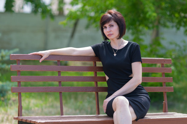 一位身穿黑色连衣裙的黑发女人下班后在公园的长椅上休息图片下载